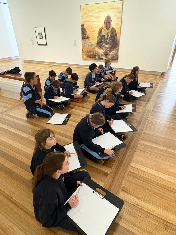 Students are seated in the National Portrait Gallery with art pad and pencil drawing a portrait. A large portrait hangs in the background.