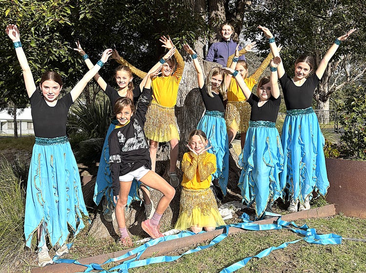 Students dressed in flowing blue and yellow costumes standing together with their arms raised.