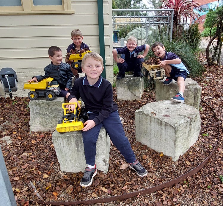 Group of boy students playing with dump truck toys around the sandstone block yarning circle.