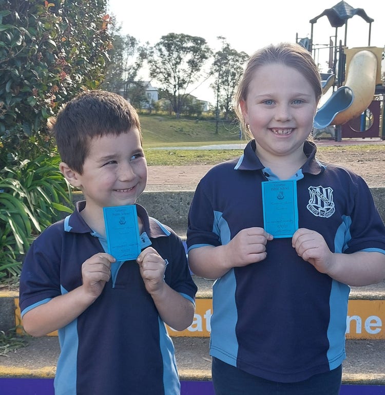 Two smiling school students holding up achievement certificates.