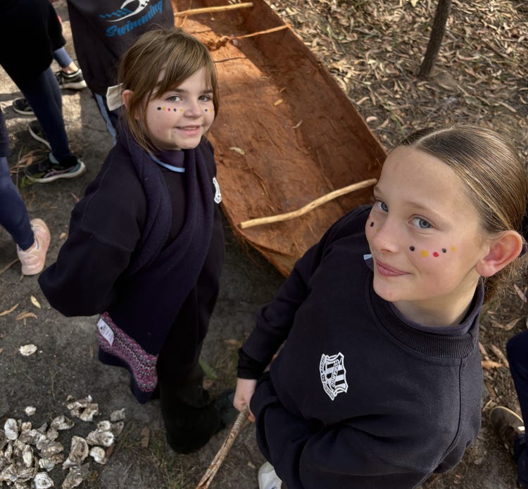 Two students with dot face paint standing next to a traditional dug out canoe.