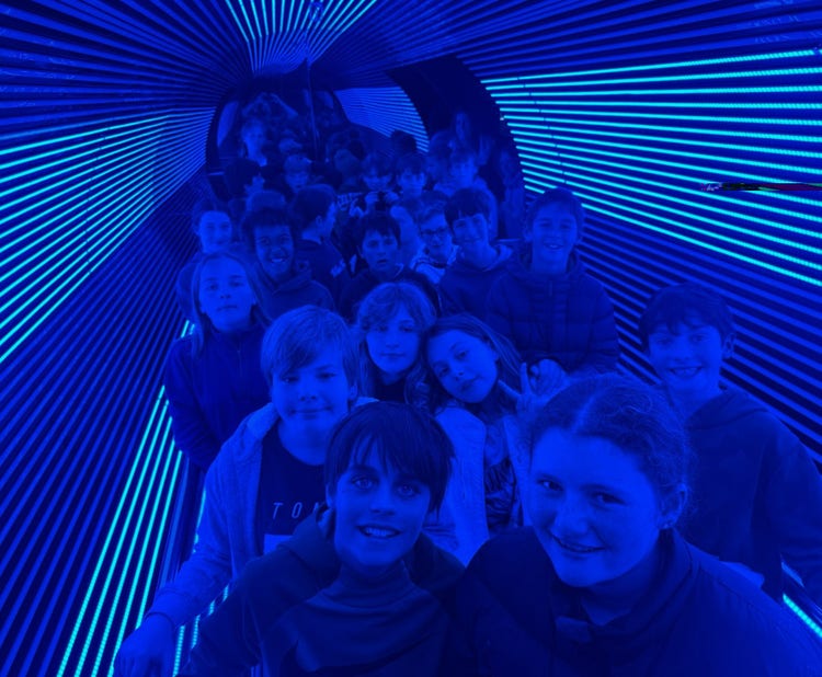Students are walking through a tunnel eluminated by blue light. They are enjoying the experience.