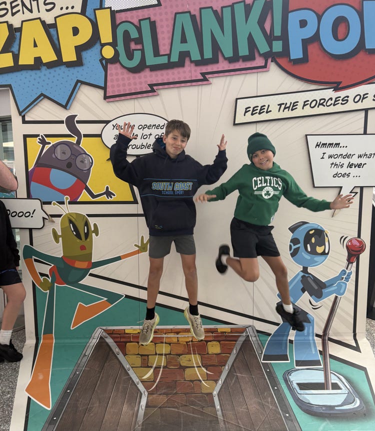 Two students are jumping in front of a pop art graphic display.