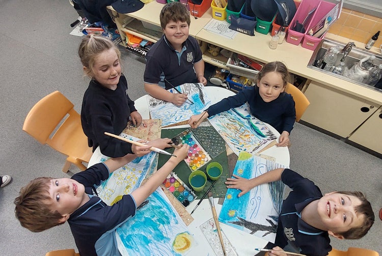Students seated around a table sharing watercolour paint palette to create paintings.