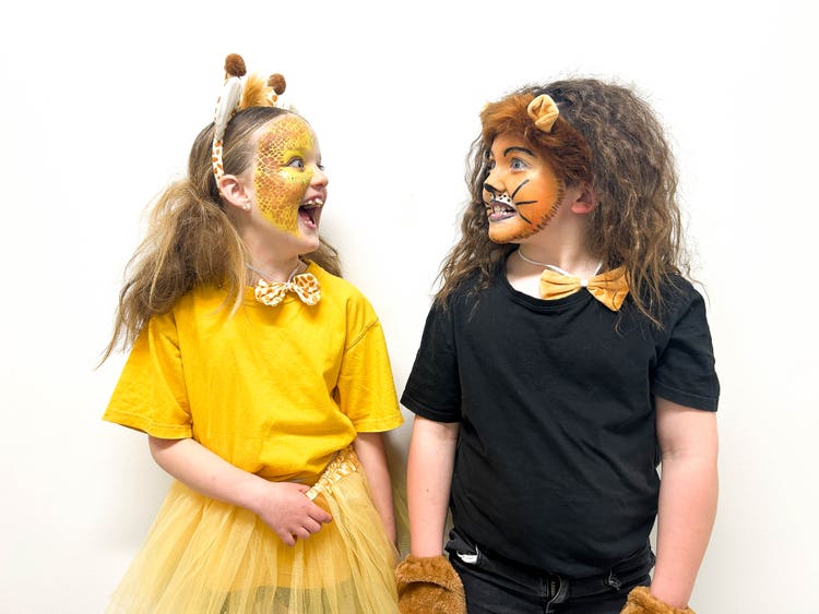 One student dressed in a yellow costume with griaffe facepaint and head band faces a student dressed in all black with a lion face paint, ears and his hair teased into a mane.