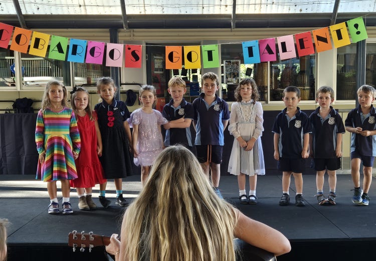 Group of young students performing together up on stage with a teacher playing guitar in front and facing them.e