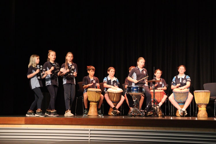 Students performing on a stage accompanied by students on Djembe drums.