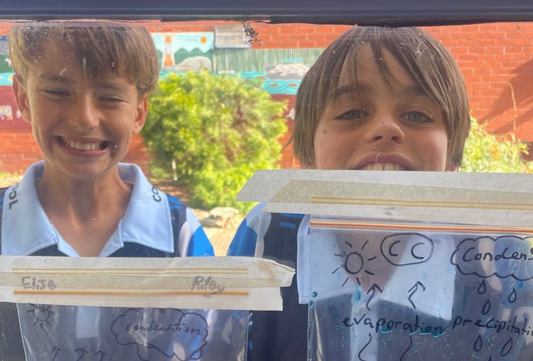 Two students looking through the window at a STEM experiment containing blue liquid.