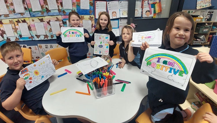 Students around a table containing colouring textas holding up positive affirmation colouring sheets.