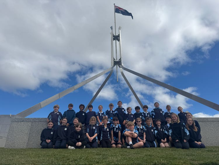 Student group gathered on the grass in front of the Parliament of Australia. The flag structure is visable behind them.