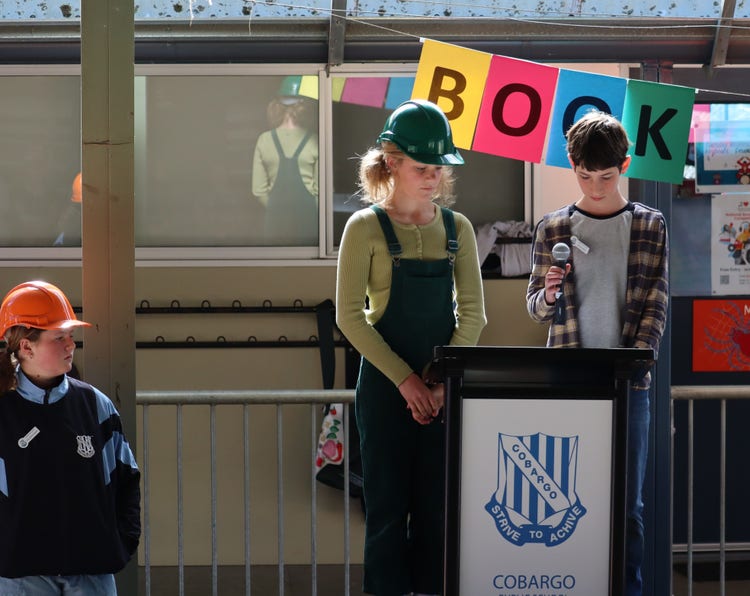 Senior students standing at the school lecturn announcing book week characters.