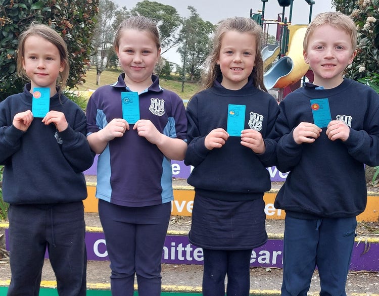 4 smiling students standing together on a step holding up a merit certificate.